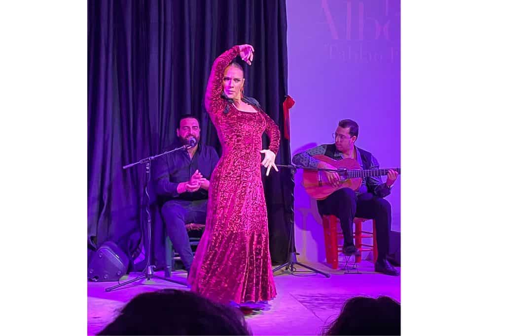 Flamenco performer in red dress with musicians, experience in Granada
