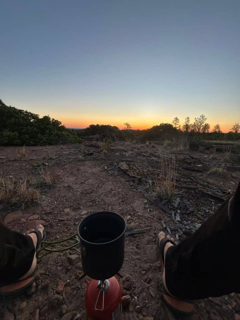 Single burner camp stove between feet at sunset