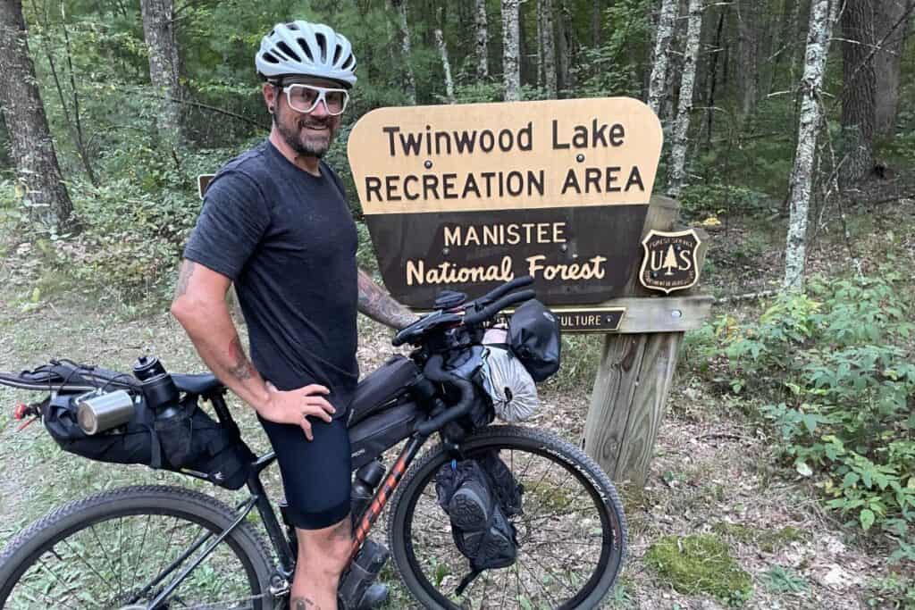 cyclist with bikepacking rig in front of rec area sign