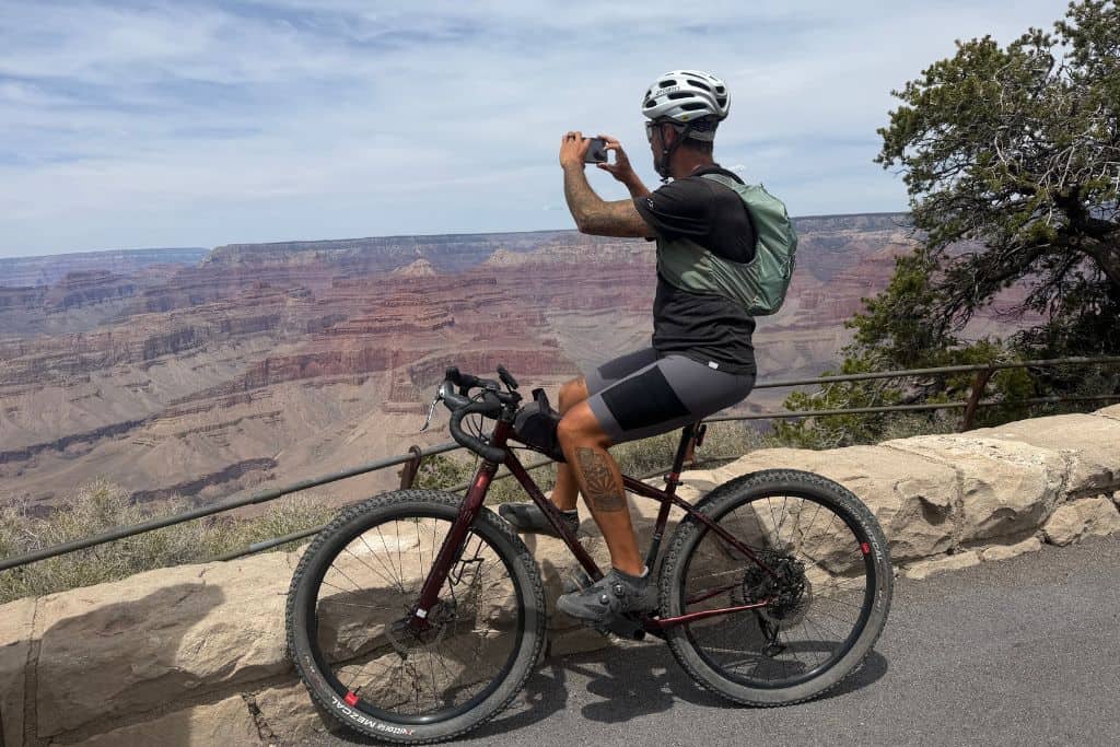 man on bicycle taking photo of Grand Canyon with running vest on