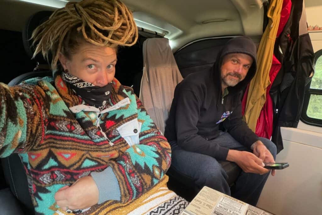 Van life couple huddled inside van with wet clothes hung in background